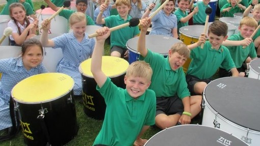 A group of pupils holding sitting with drums holding up their drum sticks 